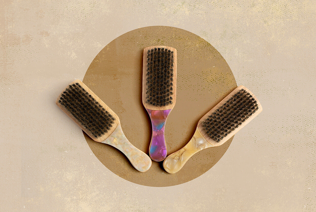 Three Lulu Travel Hair Brushes with different handle designs on a beige and gold background