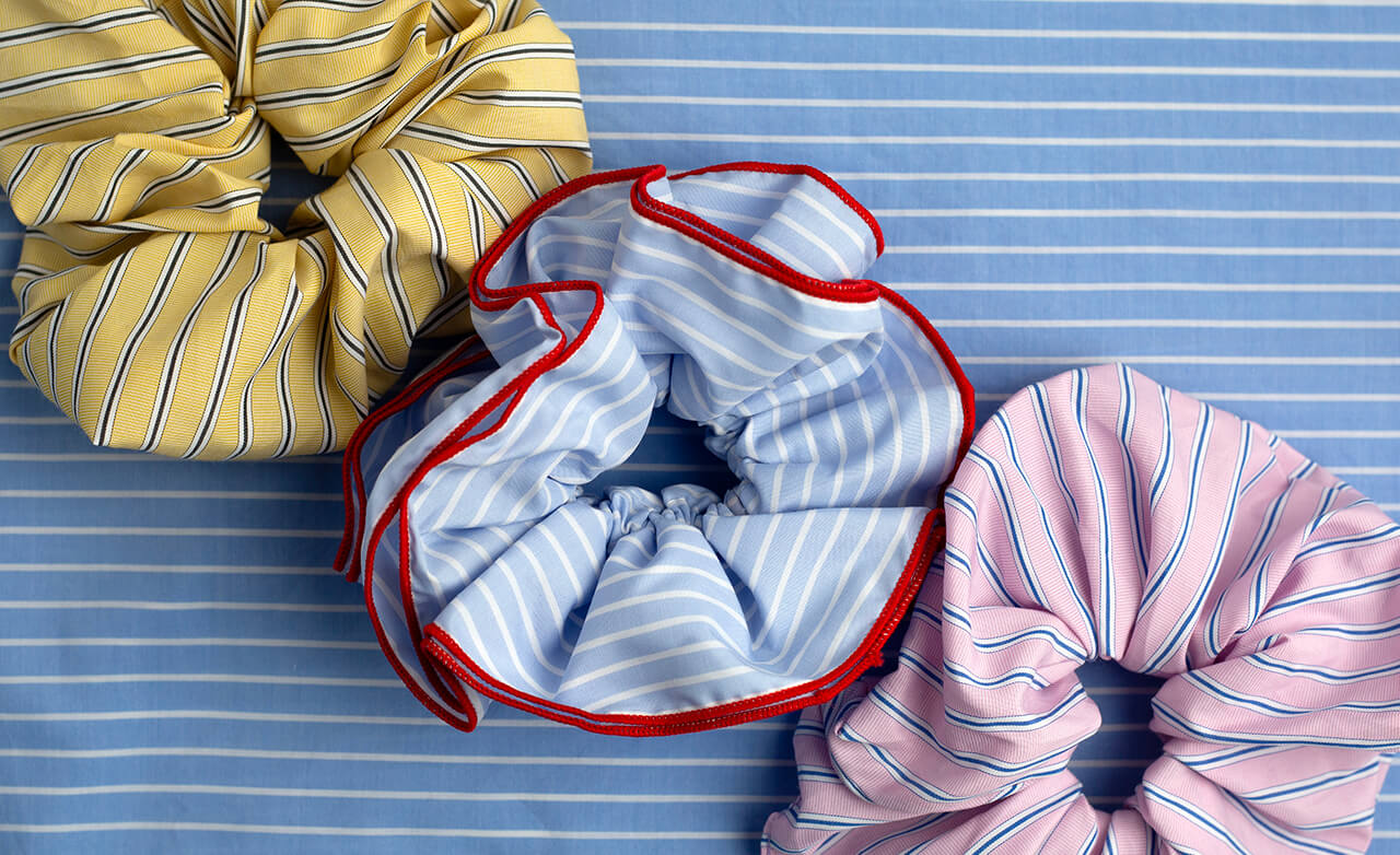 Three colourful striped scrunchies on a blue striped background
