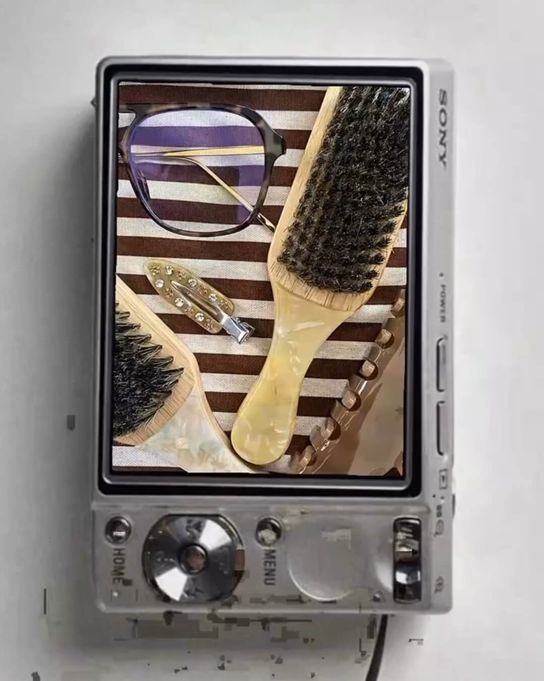 Vintage Sony digital camera with an image of a THOC travel brushes, NO Crease hair clip, caramel colour claw clips and glasses on its screen