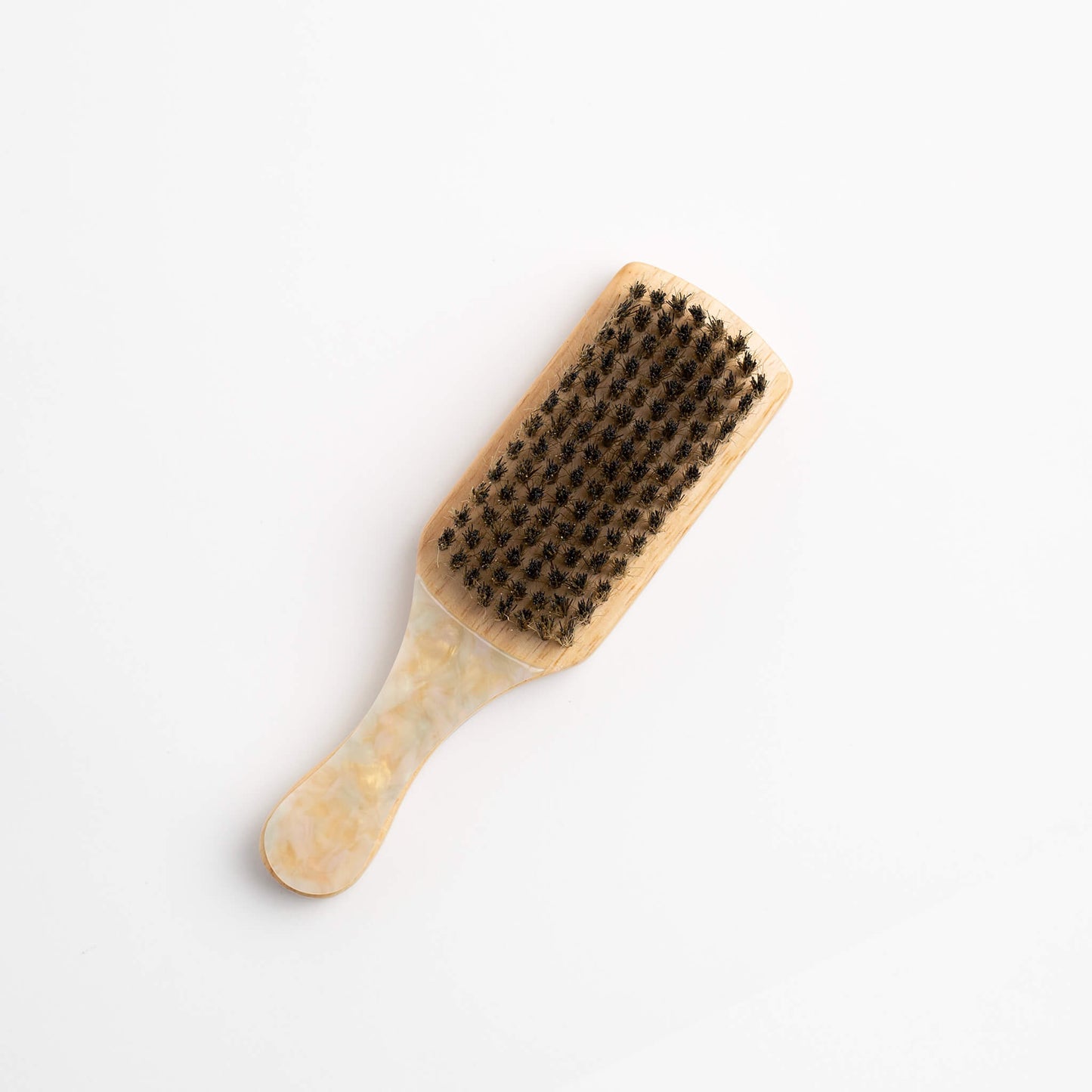 THOC Lulu Travel Brush Buttermilk with a multi-coloured purple handle, laying handle down with boar bristles up, on a white background