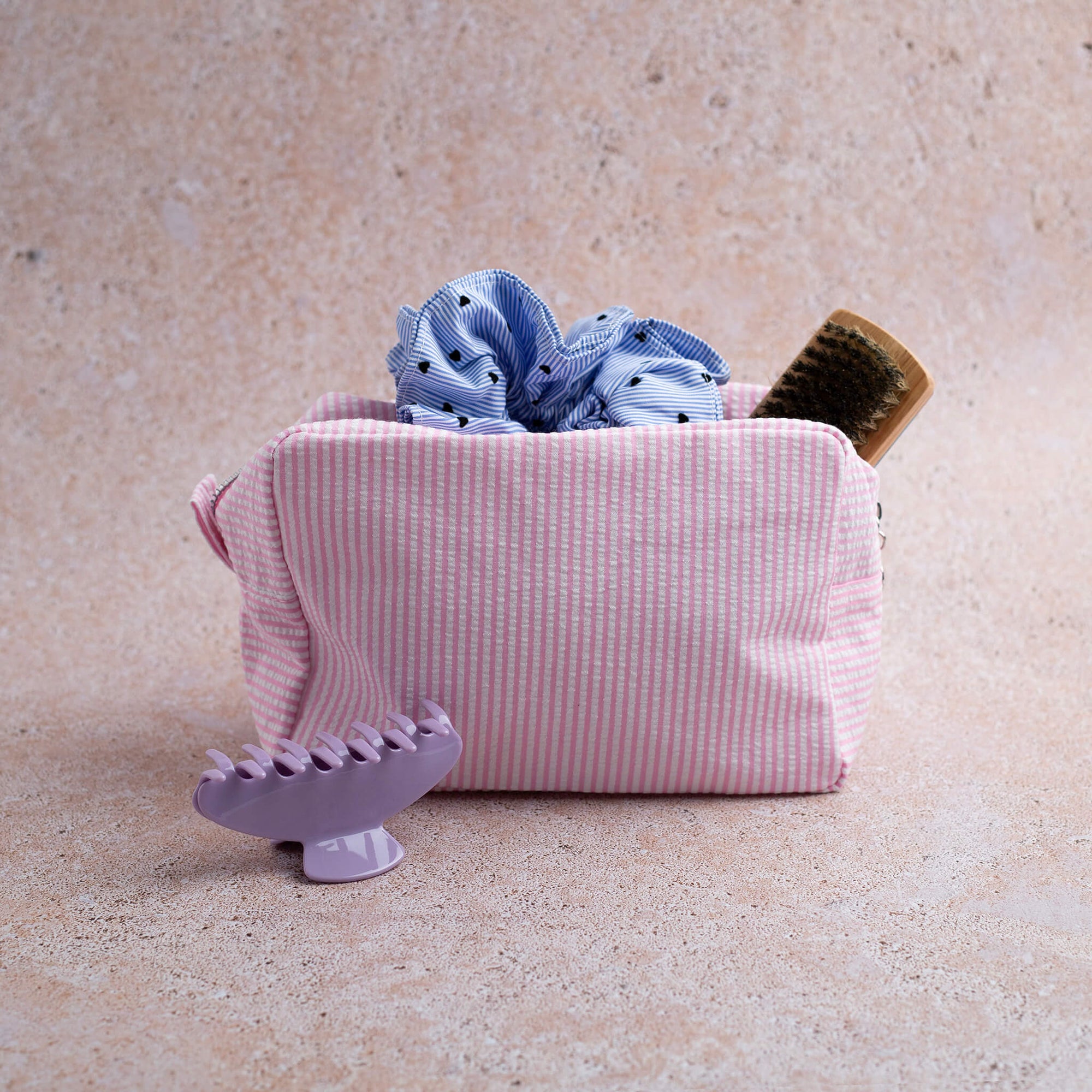 THOC Candy Beauty Bag Stripe pink, Lulu travel brush, scrunchie and claw clip  on a beige background