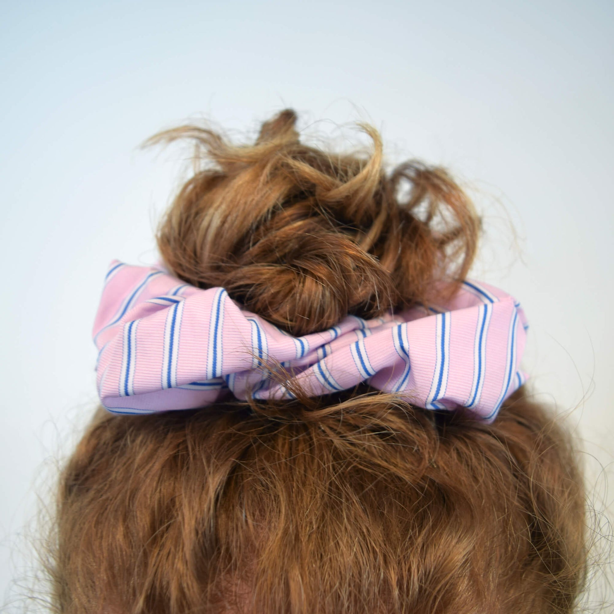 Model with red curly hair wearing THOC Blush Stripe Scrunchie in Rose Sorbet colour shown on a white background